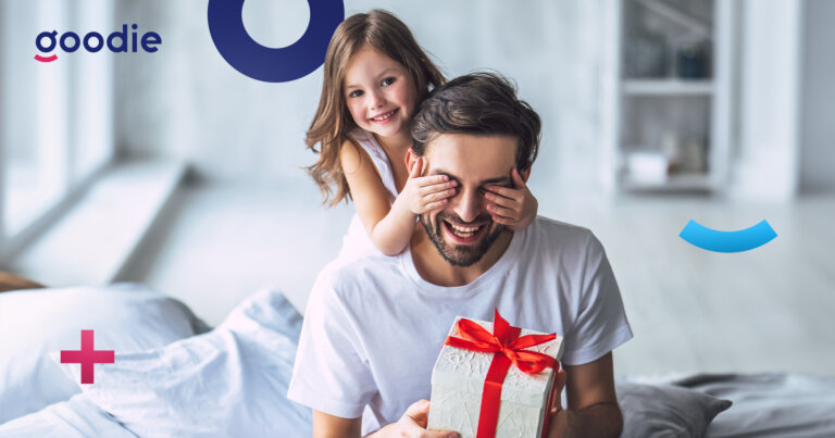 Uśmiechający się tata trzymający prezent wraz z córką. Dziewczynka przykrywa tacie oczy na znak niespodzianki na Dzień Ojca.