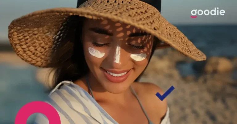 uśmiechająca się kobieta w kapeluszu z naniesionym kremem przeciwsłonecznym na policzkach i nosie, żeby ochronić się przed słońcem
